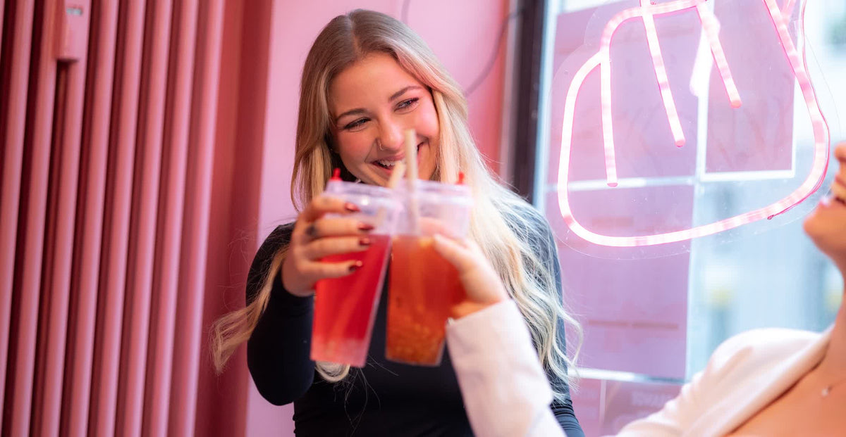 Two friends laughing and toasting with fruit tea cups