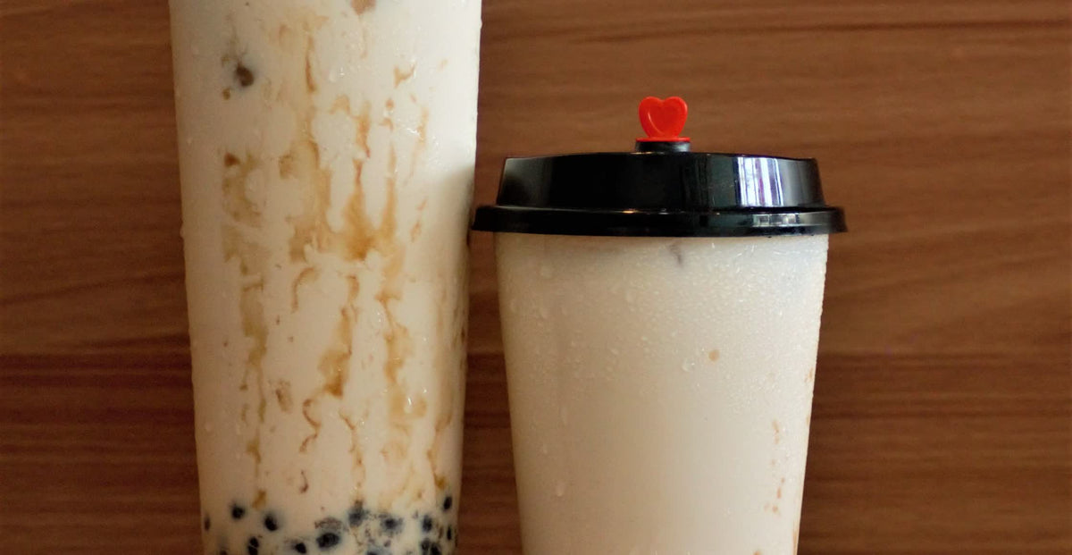 Two cups of milk tea with tapioca pearls side by side on a wooden bench