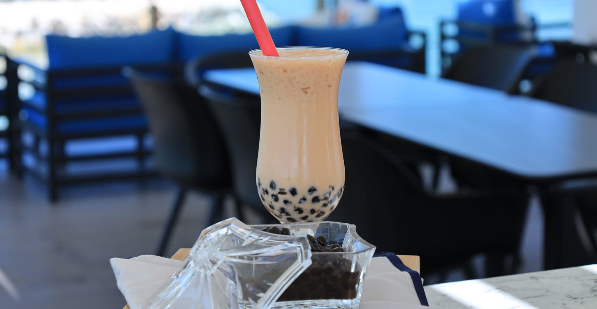 Iced milk tea with tapioca pearls in a tall glass, with a dish of pearls beside it