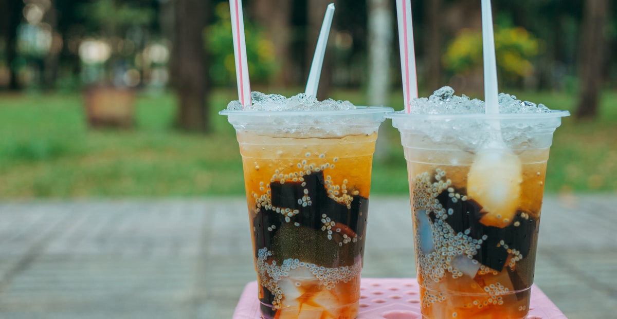 Two iced drinks with jelly toppings in plastic cups on a pink table