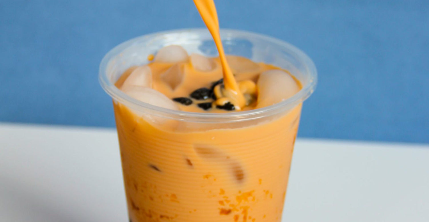Thai milk tea being poured over ice and tapioca pearls in a homemade cup