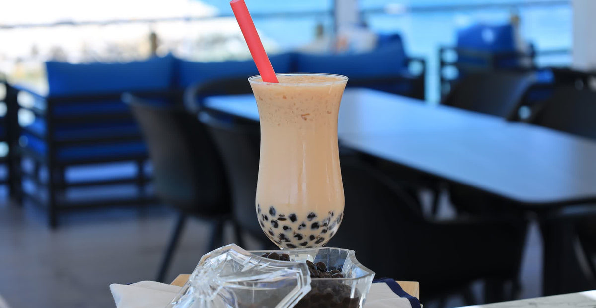 A cup of iced milk tea with tapioca pearls next to a dish of cooked pearls